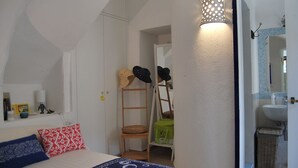 Een slaapkamer met een bed, kussens, een ladder en een wandplank met hoeden.