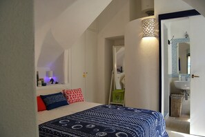 Ein Schlafzimmer mit einem Bett, einem Nachttisch, einer Lampe und einem durchgehenden Türspalt sichtbaren Badezimmer.