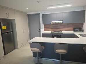A modern kitchen with a central island, bar stools, a built-in microwave, and a stainless steel refrigerator. - Charming 2BR + 2BA in Panama City's most luxurious building ✨🏙️🏊 (El Cangrejo)