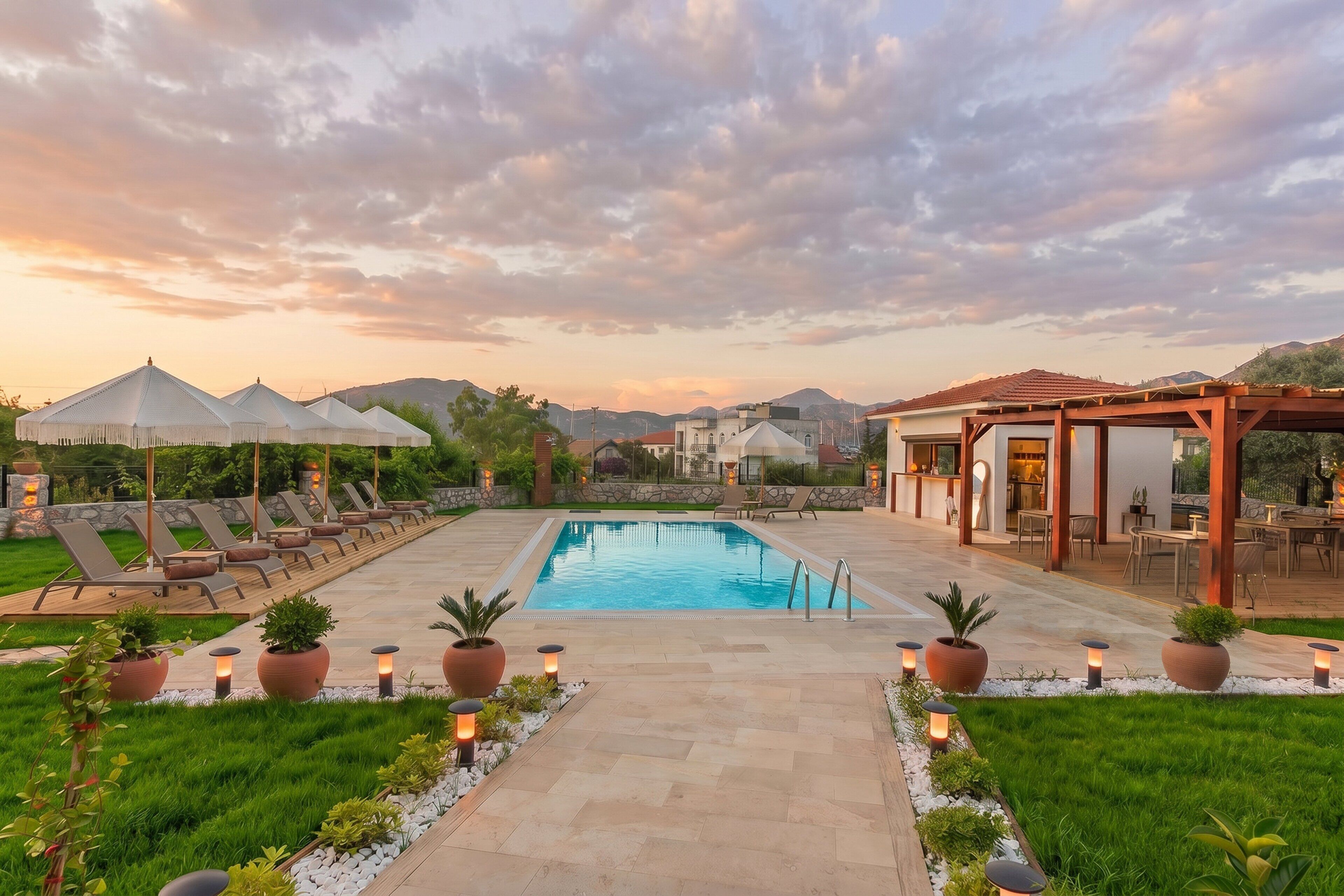 Piscina com espreguiçadeiras e guarda-sóis, cercada por vegetação e um caminho de pedra.