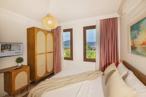 Un dormitorio con cama, armario de madera, televisor, ventana con vistas y un cuadro en la pared.