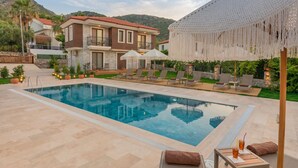 A swimming pool with lounge chairs and umbrellas, a house with a red roof, and a mountainous backdrop. - Kiraz Vela Selimiye (Marmaris)