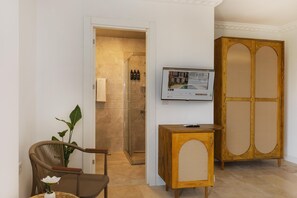 A modern bathroom with a glass shower enclosure, a wooden cabinet with a woven front panel, and a small table with a remote control. - Kiraz Vela Selimiye (Marmaris)