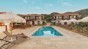 A pool area with lounge chairs and umbrellas, surrounded by two-story buildings with balconies. - Kiraz Vela Selimiye (Marmaris)
