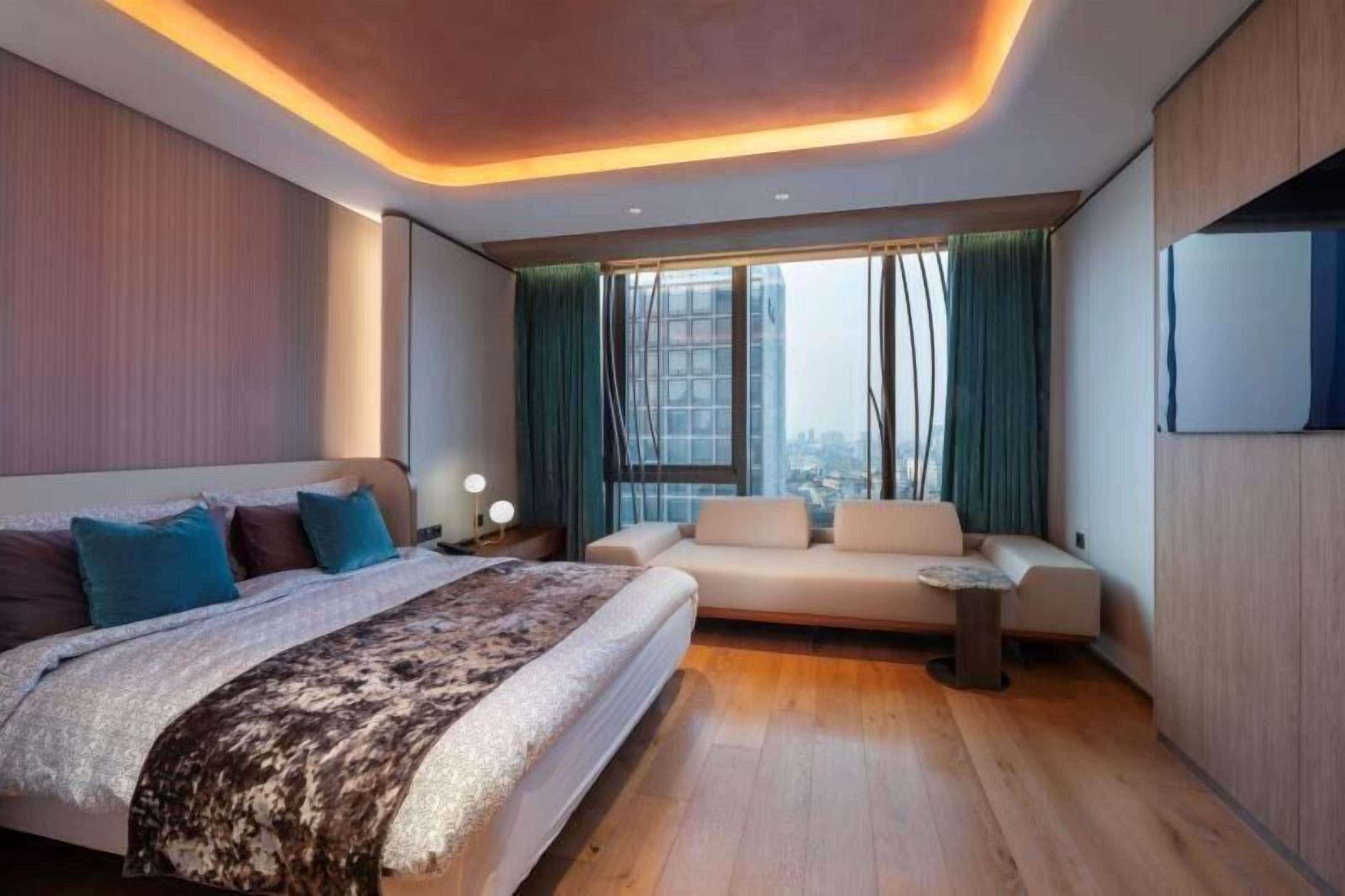 Habitación de hotel moderna con una cama grande, un sofá, una mesita y vistas a la ciudad.