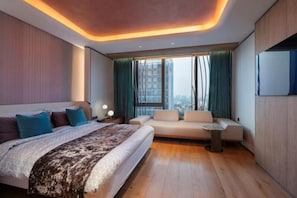 Habitación de hotel moderna con una cama grande, un sofá, una mesita y vistas a la ciudad.