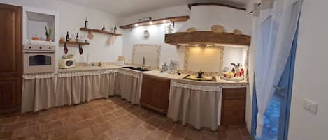 A kitchen with a built-in oven, a microwave, and a stove. There are wooden shelves above the counter holding various kitchen items.