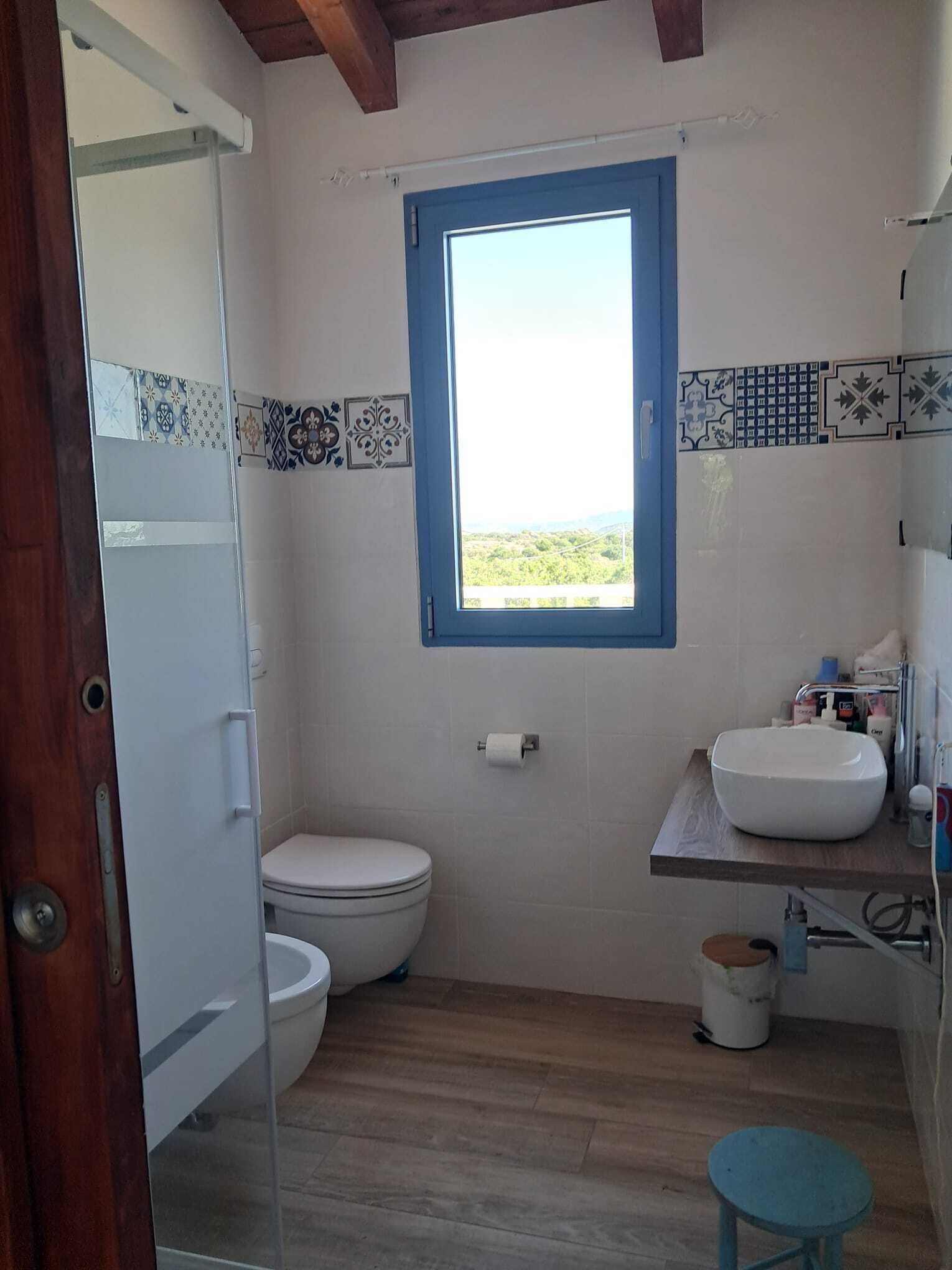 A bathroom with a toilet, a sink, a window, and a small stool.