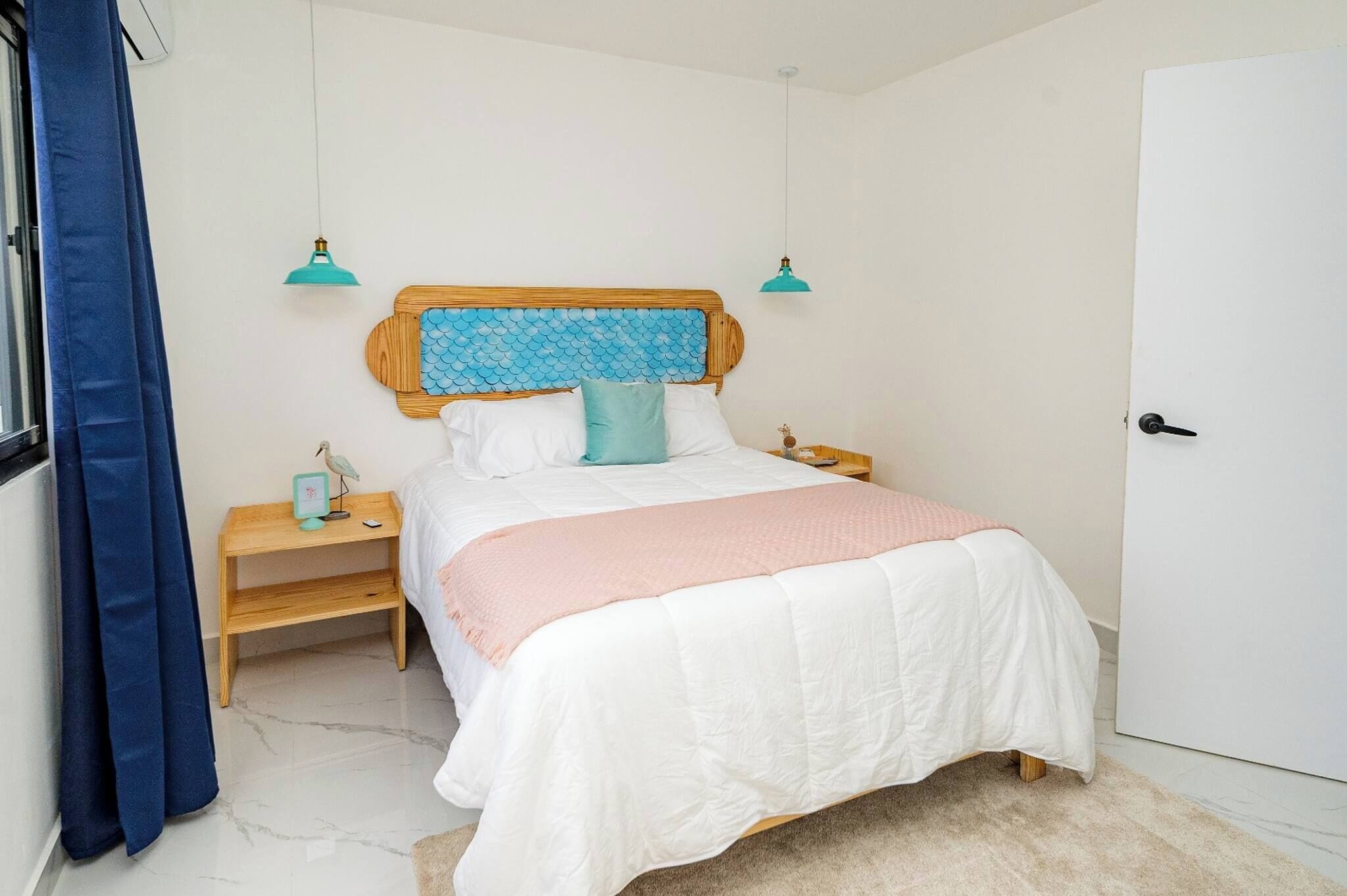 A bedroom with a bed, bedside tables, a nightstand, a door, and a window with curtains.