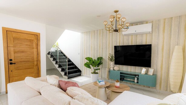 A modern living room with a sofa, a television, a staircase, and a plant. - Villa for 7 People in Punta Cana (Punta Cana)