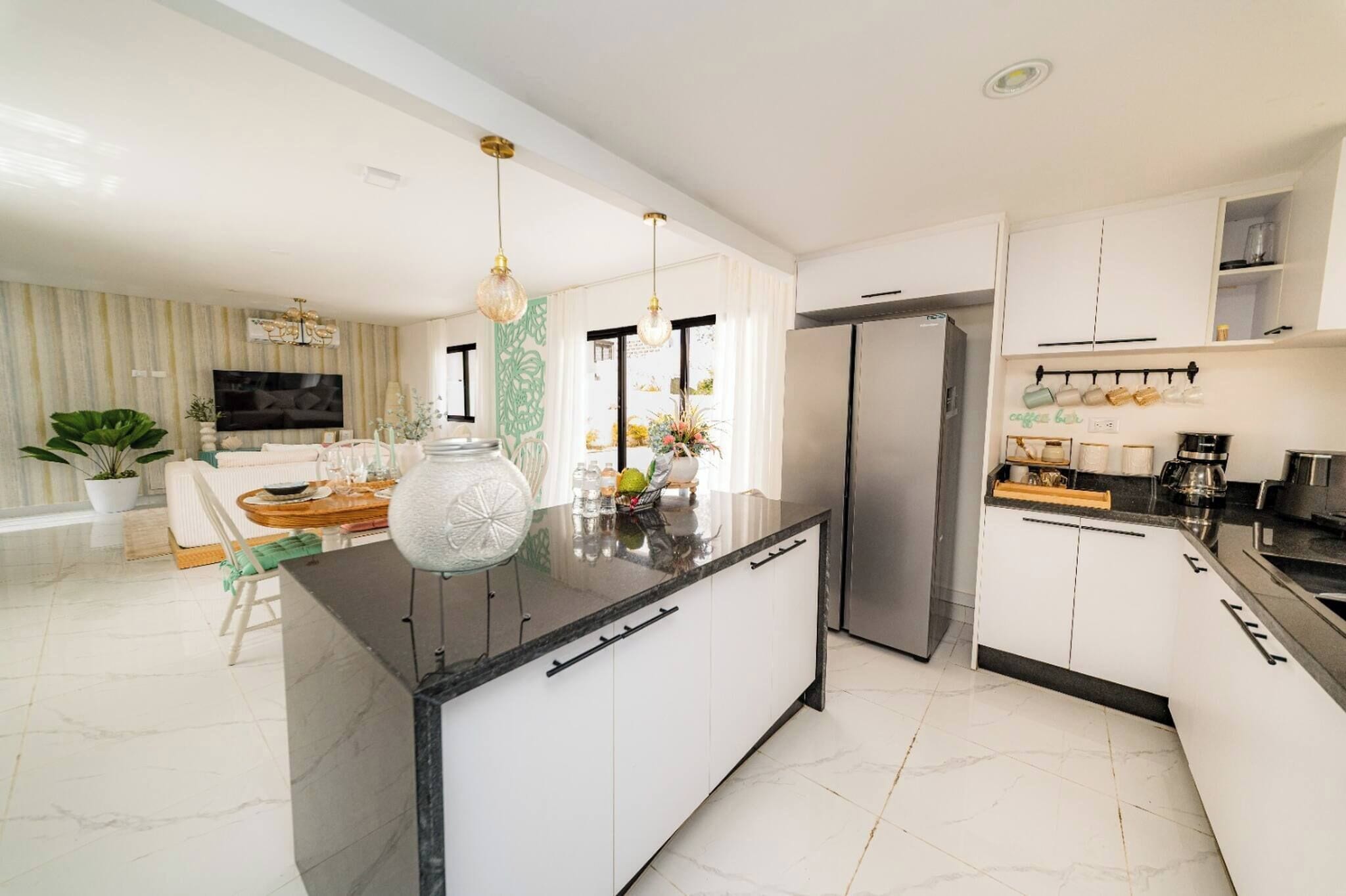 Una cocina moderna con una isla central, electrodomésticos de acero inoxidable y un comedor con un sofá blanco y una planta grande en maceta.
