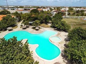 A large swimming pool with a wavy edge, surrounded by trees and a view of a residential area in the background. - Villa for 7 People in Punta Cana (Punta Cana)