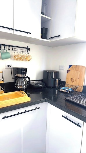 A modern kitchen with white cabinets, a black countertop, a coffee maker, a toaster, and a wooden cutting board. - Villa for 7 People in Punta Cana (Punta Cana)