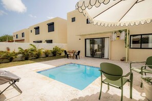 A swimming pool with a tiled edge, surrounded by a patio area with outdoor furniture. - Villa for 7 People in Punta Cana (Punta Cana)