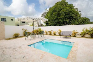A swimming pool with two chairs and a table, surrounded by plants and a white wall. - Villa for 6 People in Punta Cana (Punta Cana)