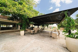 Un espacio de patio al aire libre con mesas y sillas, rodeado de vegetación y una sección cubierta.