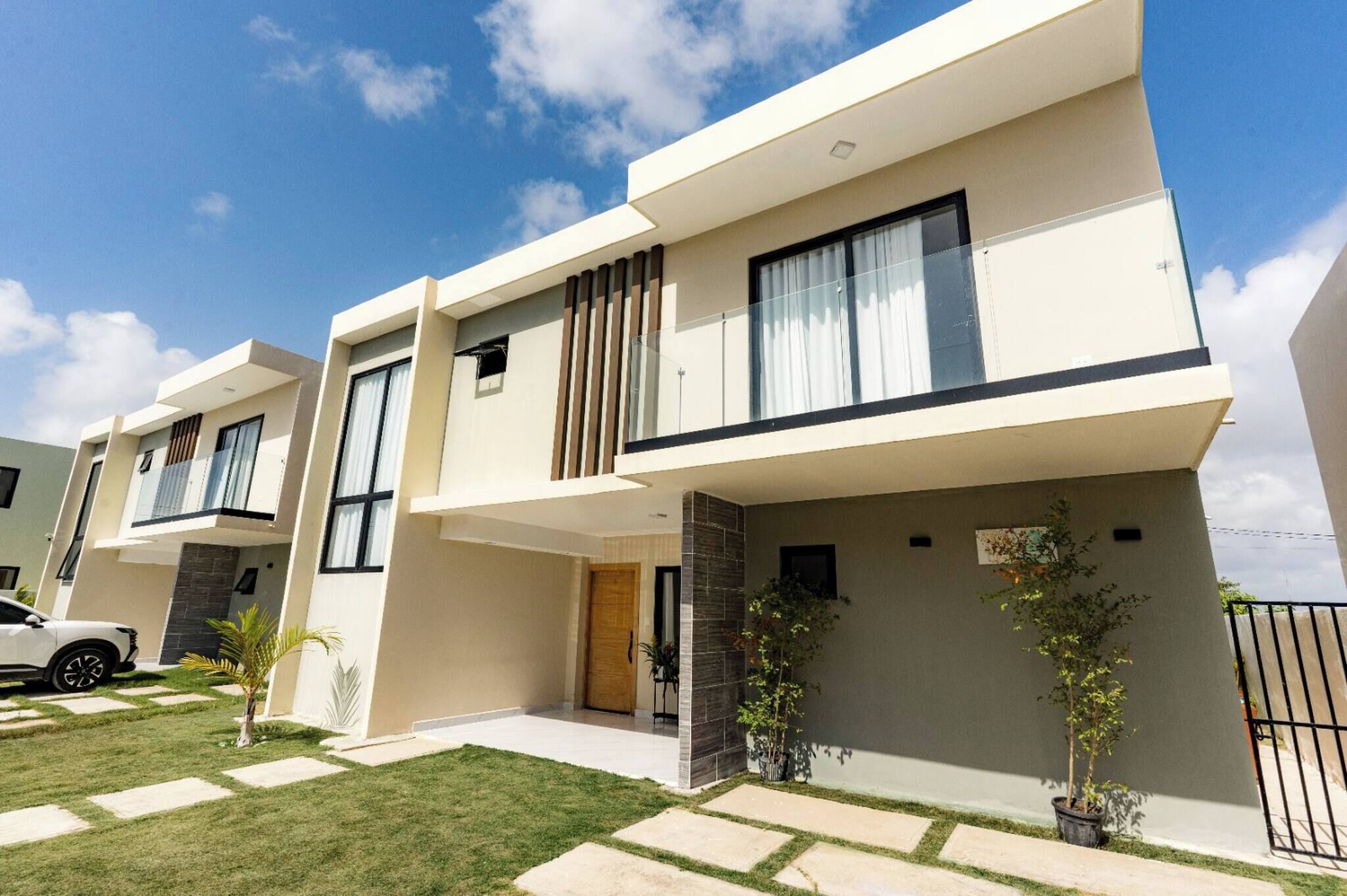 A modern two-story residential building with a flat roof, large windows, and a well-maintained lawn.