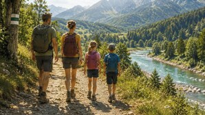 Una familia camina por un sendero de tierra junto a un río, con montañas al fondo.