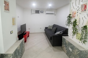 Ein Wohnzimmer mit einem dunklen Sofa, einem roten Couchtisch, einem Flachbildfernseher und einer wandmontierten Klimaanlage.