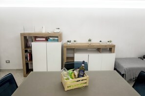 Ein Zimmer mit Esstisch, einer Holzkommode mit Glasplatte und einem kleinen Topfpflanz.