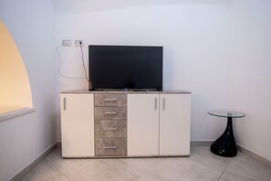 Ein modernes Zimmer mit Flachbildfernseher auf einer Kommode, einem kleinen Glastisch und einer Steckdose.