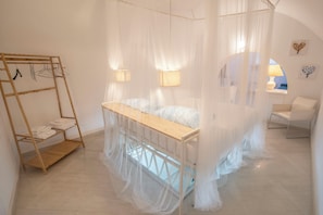 A bedroom with a canopy bed, a wooden shelf with towels, and a chair. - La Casa di Ale in Chiaja: a comfortable and modern apartment in the heart of the city. (Napoli)