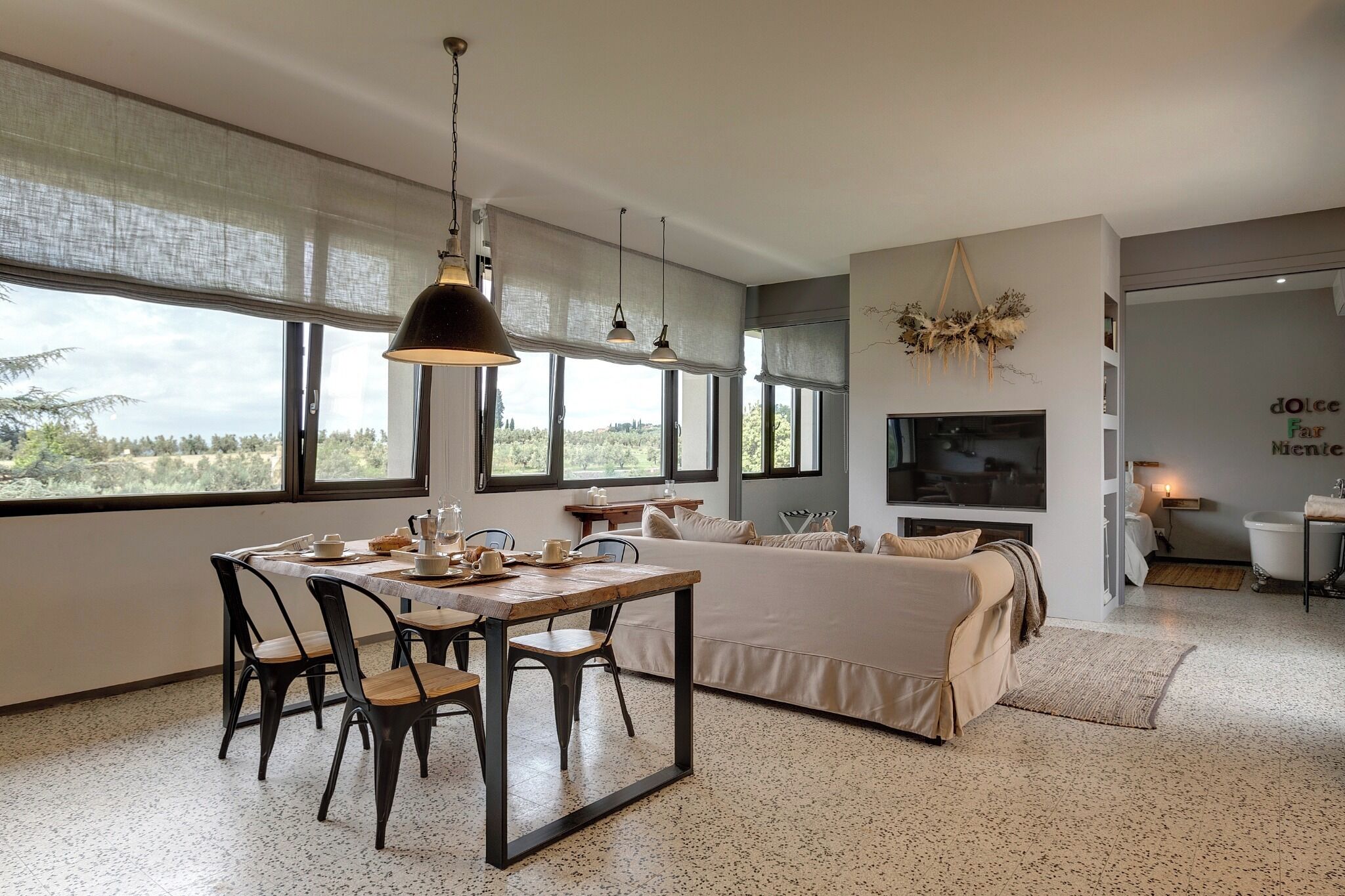Ein modernes Wohnzimmer mit großem Fenster, einem Essbereich mit Tisch und Stühlen, einer Couch und einem an der Wand montierten Fernseher.