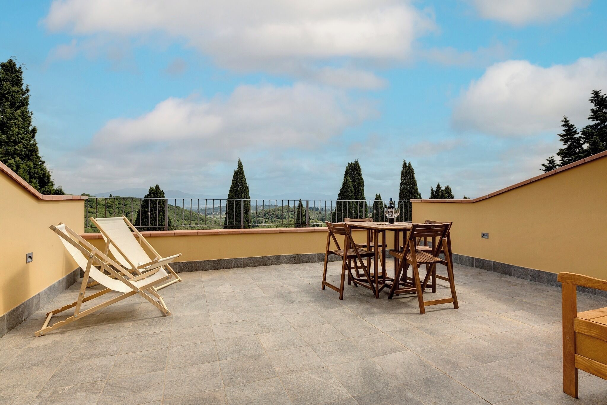 A rooftop terrace with a table and chairs, a wooden chair, and a view of the surrounding landscape.