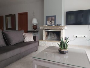 A living room with a sofa, a fireplace, a television, and a potted plant. - Villa Marilena at Nafpaktos. (Paleopanagia)