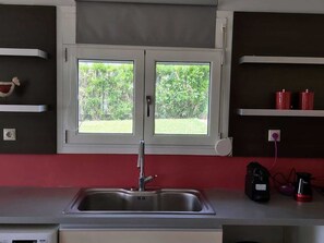 Una cocina con un lavamanos doble, una ventana con vista a la vegetación y estanterías rojas.