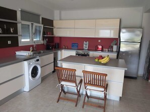Een moderne keuken met een ingebouwde wasmachine, een centraal kookeiland met zitplaatsen, en een roestvrijstalen koelkast.