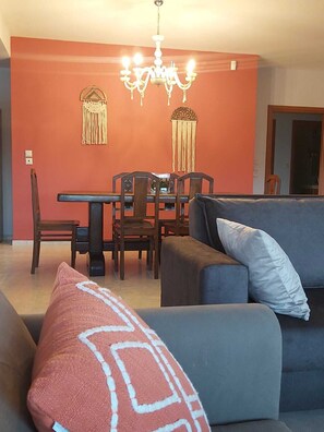 Una sala de estar con un sofá, una mesa de comedor con sillas y una araña.