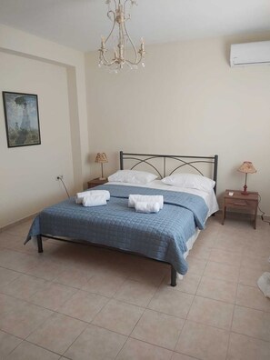 Un dormitorio con cama, dos mesitas de noche, una araña, aire acondicionado y un cuadro en la pared.