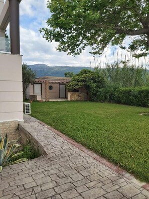 Una propiedad residencial con un sendero pavimentado que conduce a una casa de techo con tejas, rodeada de un césped bien cuidado y con una montaña al fondo.