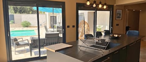 A modern kitchen with a large island, a built-in oven, and a view of an outdoor pool area.