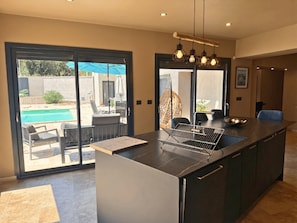 A modern kitchen with a large island, a built-in oven, and a view of an outdoor pool area. - Family Home in Provence (Piolenc)