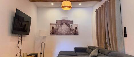 A modern living room with a sofa, a flat-screen TV, a painting, and a wooden ceiling beam.