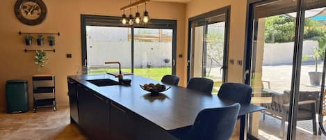 A modern kitchen with a central island, bar stools, a large window, and a view of the outdoors.