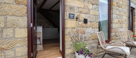 A stone building with a wooden door leading to a kitchen, a sign reading 'Wren's Nest,' and wicker chairs outside.