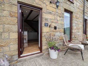 A stone building with a wooden door leading to a kitchen, a sign reading 'Wren's Nest,' and wicker chairs outside. - Wren's Nest (Whitby)