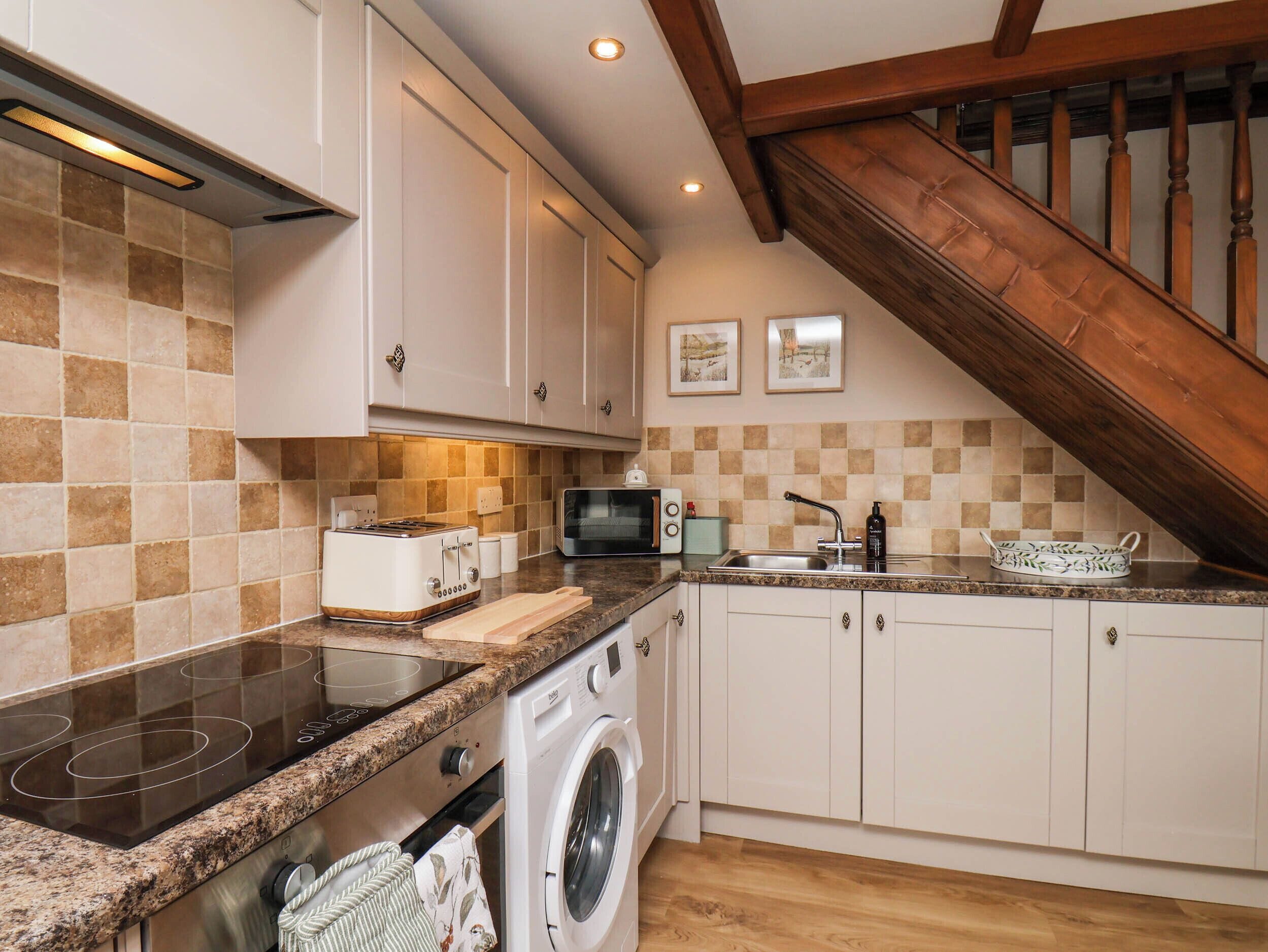 A kitchen with a built-in stove, microwave, and washing machine, wooden staircase, and tiled backsplash.