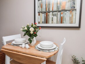 A dining table with white plates and a vase of flowers, set against a wall with a framed book collection. - Wren's Nest (Whitby)