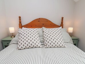 A bed with a wooden headboard, two bedside tables with lamps, and striped bedding. - Wren's Nest (Whitby)