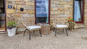 A stone building with two wicker chairs and a small table, a potted plant with purple flowers, and a sign reading 'Wren's Nest.' - Wren's Nest (Whitby)