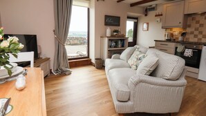 A cozy living room with a sofa and a television, a kitchen with cabinets and a stove, and a view through a window. - Wren's Nest (Whitby)