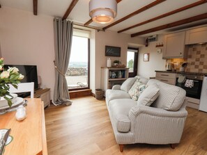 Ein gemütliches Wohnzimmer mit einer Couch und Fernseher, eine Küche mit Schränken und Herd, und ein Ausblick durch ein Fenster.