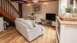 A cozy living room with a wooden staircase, a striped sofa, a television, and a wicker basket with eggs. - Wren's Nest (Whitby)