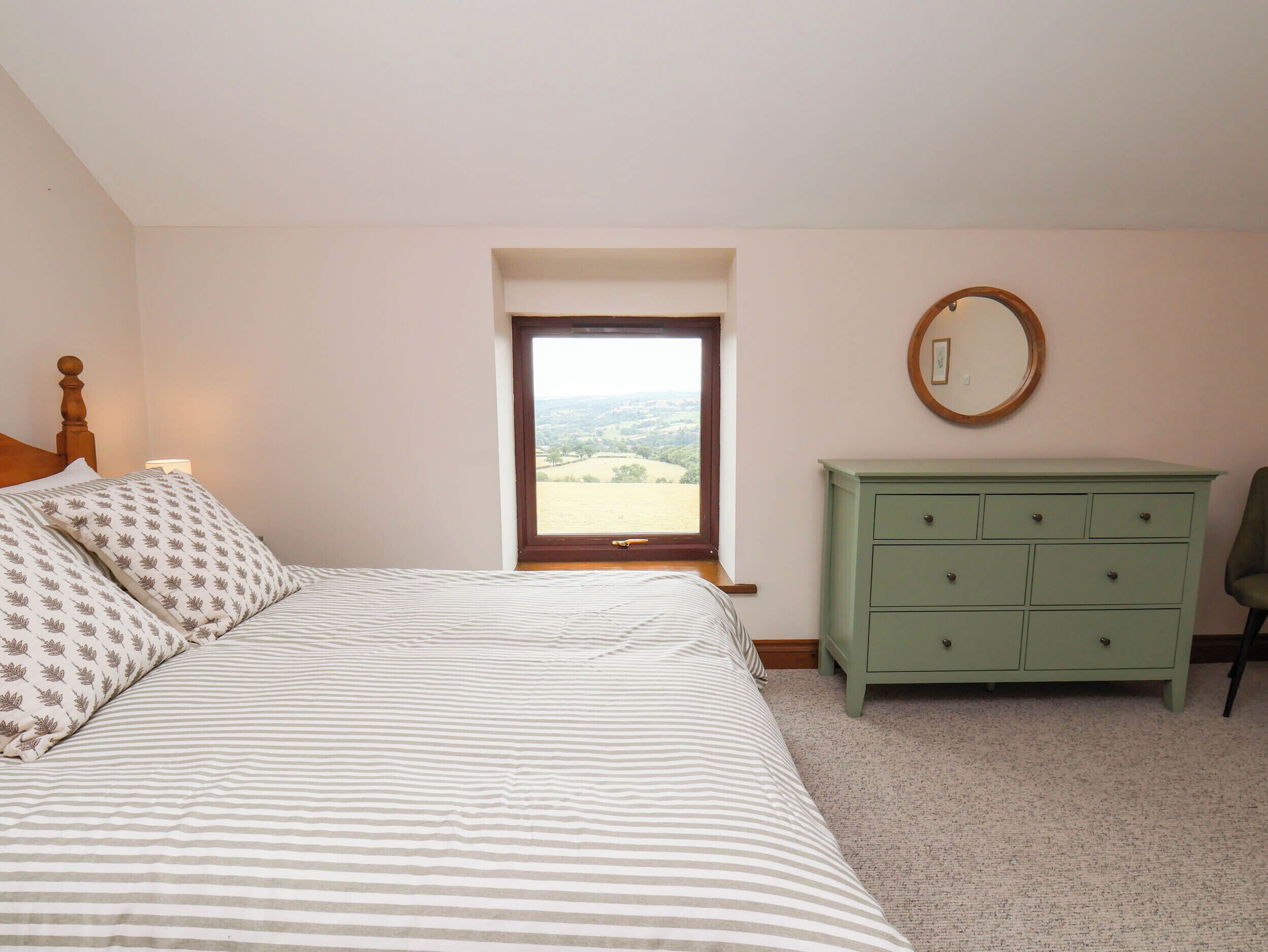 A bedroom with a bed, a dresser, a mirror, and a window with a view.