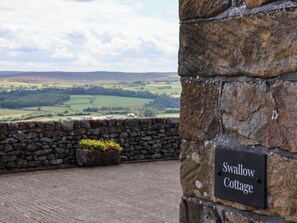 Eine Steinsäule mit einem Schild, auf dem 'Swallow Cottage' steht, und im Hintergrund grüne Felder.
