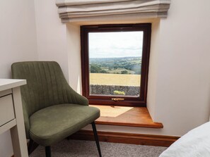 Ein Zimmer mit einem einzelnen grünen Sessel, einer hölzernen Bank und einem Fenster zur Steinwand.